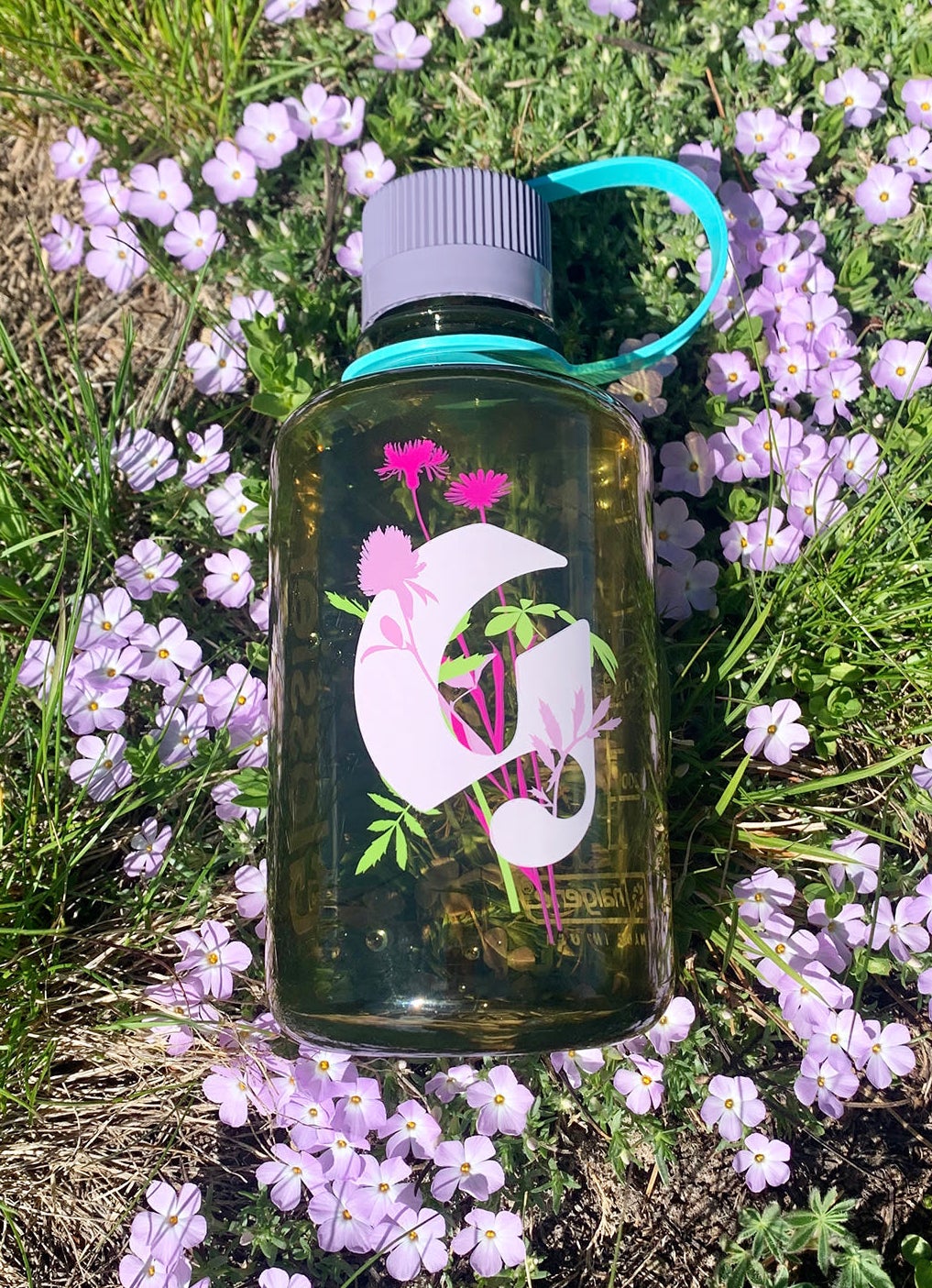 The semi-clear green water bottle with a floral Glossier g logo in pink with flowers on it on the front and grey lid with teal strap
