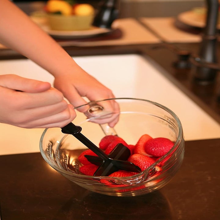 Hand uses same black food chopper to mash up strawberries in a glass bowl