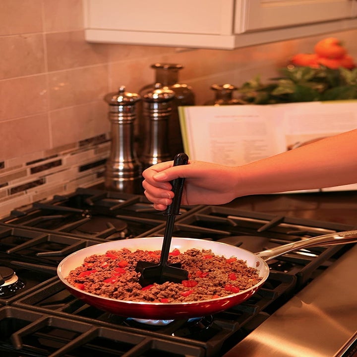 Hand uses black food chopper to mash up ground beef in a skillet