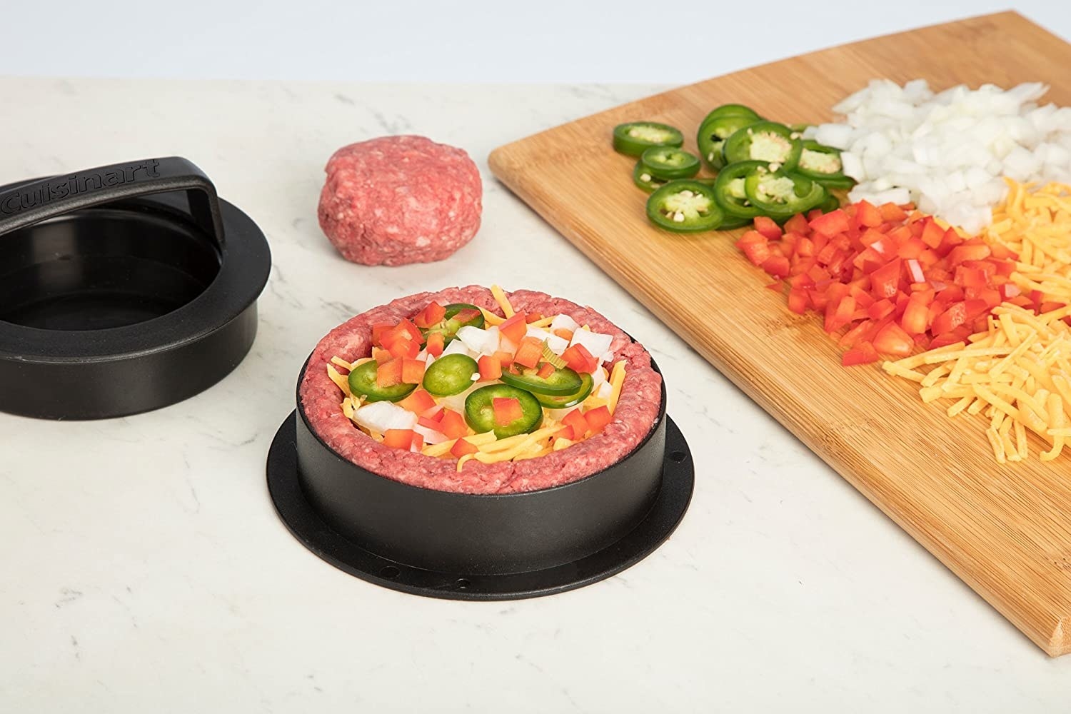 Black four-in-one burger press with ground meat, jalapeños, cheese, and onions inside