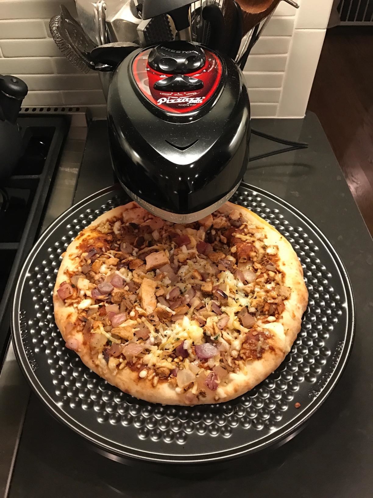 Reviewer shows meat and cheese-covered pizza made with gray rotating pizza oven 