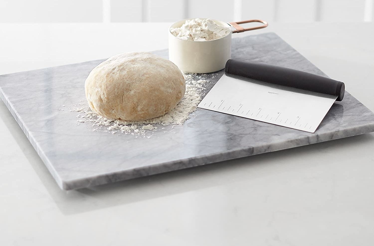 Dough sitting on a marble board with a bench scraper beside it