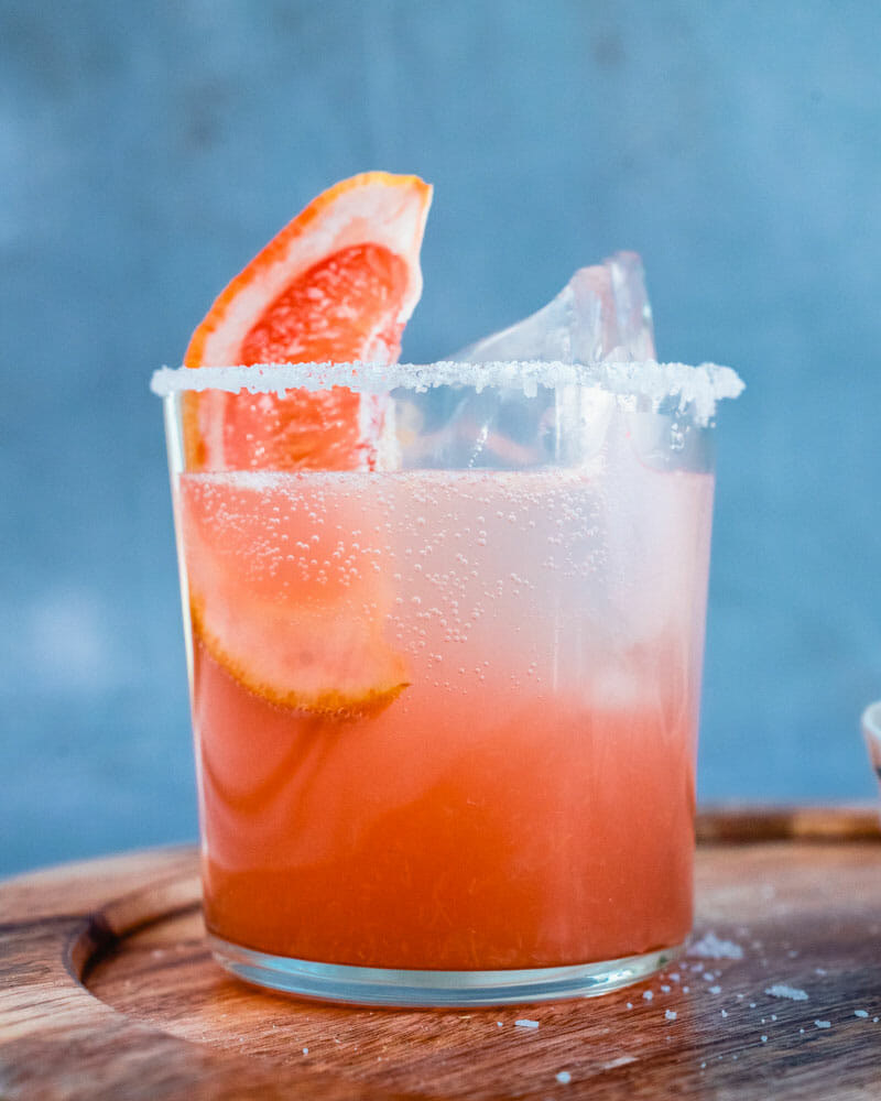 A Paloma cocktail with a salted rim and slice of grapefruit on the edge of the glass.