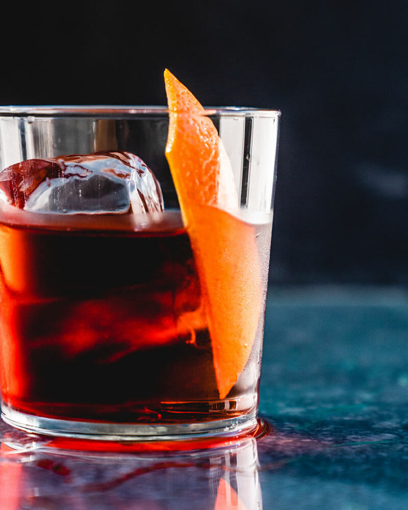 A whiskey Negroni (aka a Boulevardier) cocktail with an ice cube and orange peel.