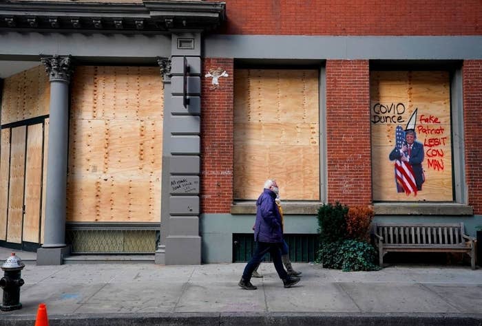 A couple walking past boarded up shop windows with anti-Trump graffiti on them