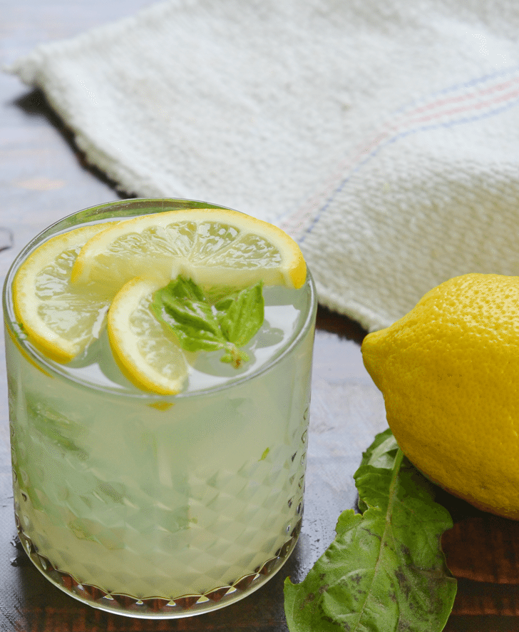 A lemon basil gin fizz on a tabletop with a lemon and a piece of basil beside it.
