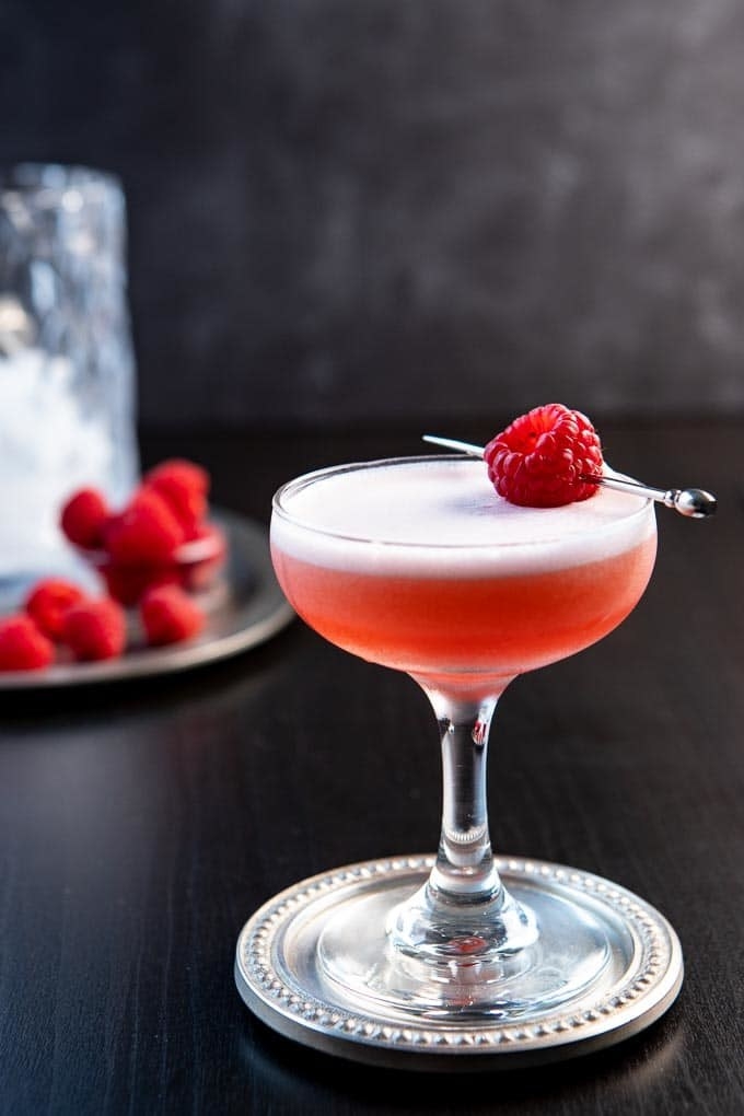 A clover club cocktail with a fresh raspberry garnish in a coupe glass.