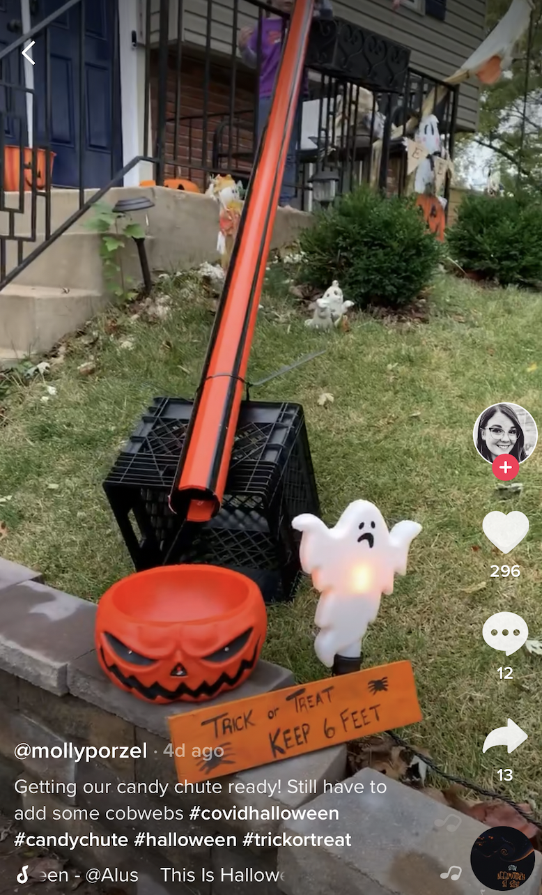 Candy chute that leads down to an angry pumpkin-shaped bowl next to a sign decorated with spiders and says &#x27;Trick or Treat, Keep 6 Feet&#x27;