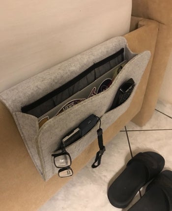 reviewer's gray bedside caddy hooked on the side of a bed 