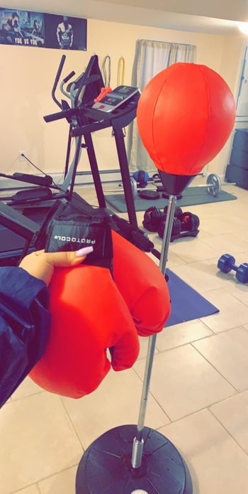 Reviewer holds red gloves in front of red and silver punching bag stand in home gym