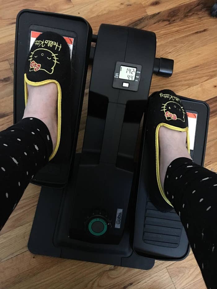 Reviewer pedals feet on black desk elliptical while wearing Hello Kitty slippers