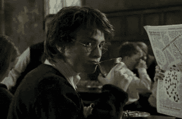 GIF of Harry Potter accidentally spitting a drink in awe as he sits in the Great Hall