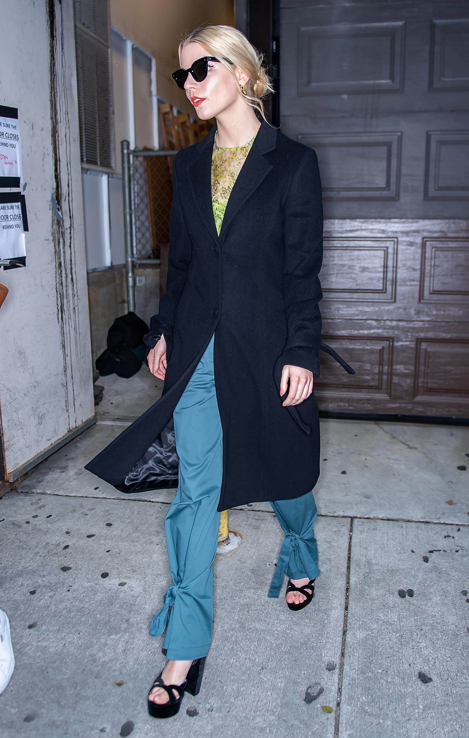 Anya Taylor-Joy walking in a long coat, sunglasses, and platform heels