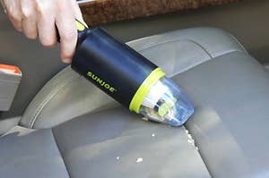 person using a small handheld cleaner to vacuum up crumbs in a car seat