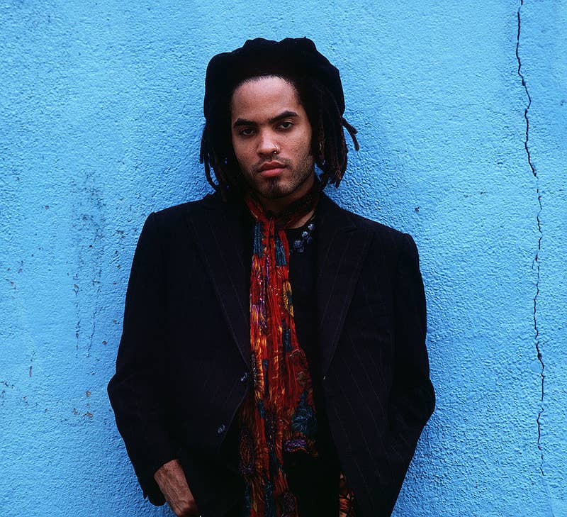 Lenny Kravitz posing in front of a blue wall in 1989 while wearing a hat and colorful scarf