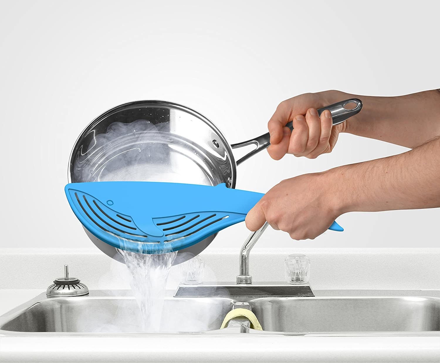 A blue whale-shaped strainer held against a pasta pot to drain water 