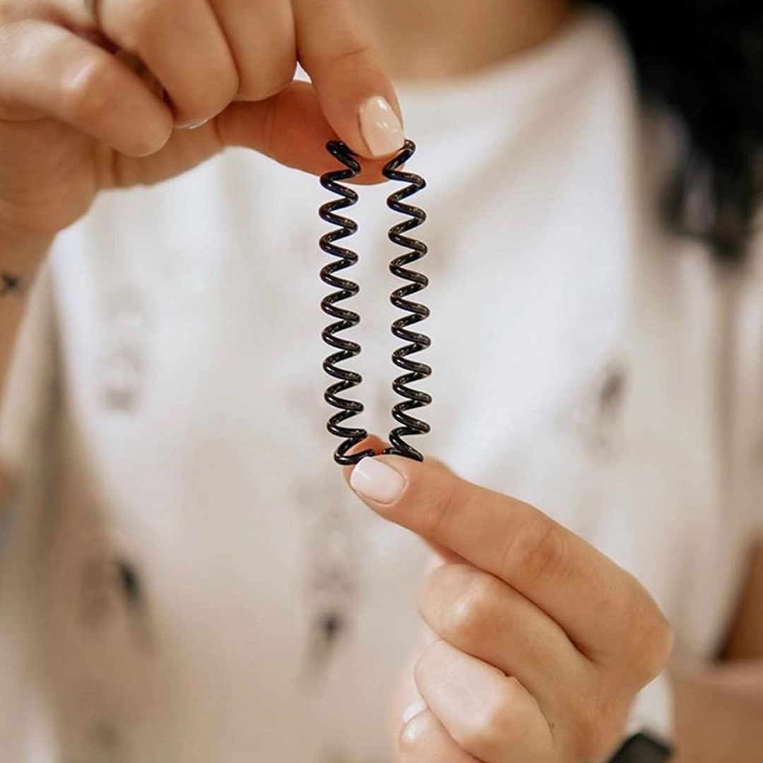 A model stretching a brown spiraled hair tie between their fingers 