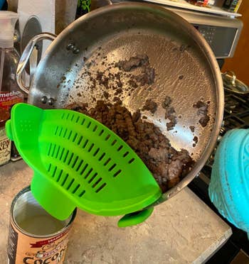 A reviewer draining the grease out of a pan of ground meat with the green colander