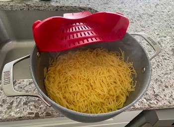 The red colander clipped onto the side of a pot of spaghetti 