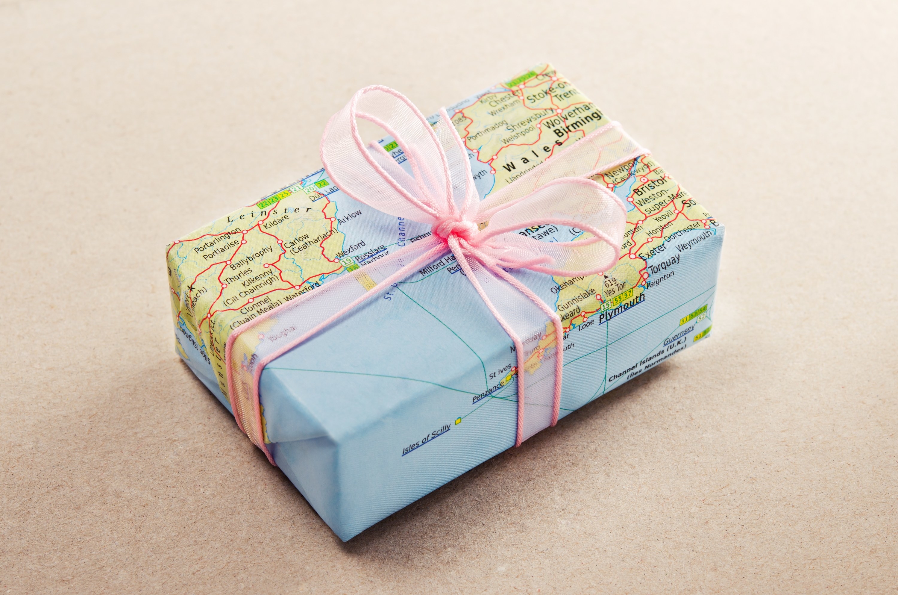 Small gift wrapped in a colorful map with a pink bow. 