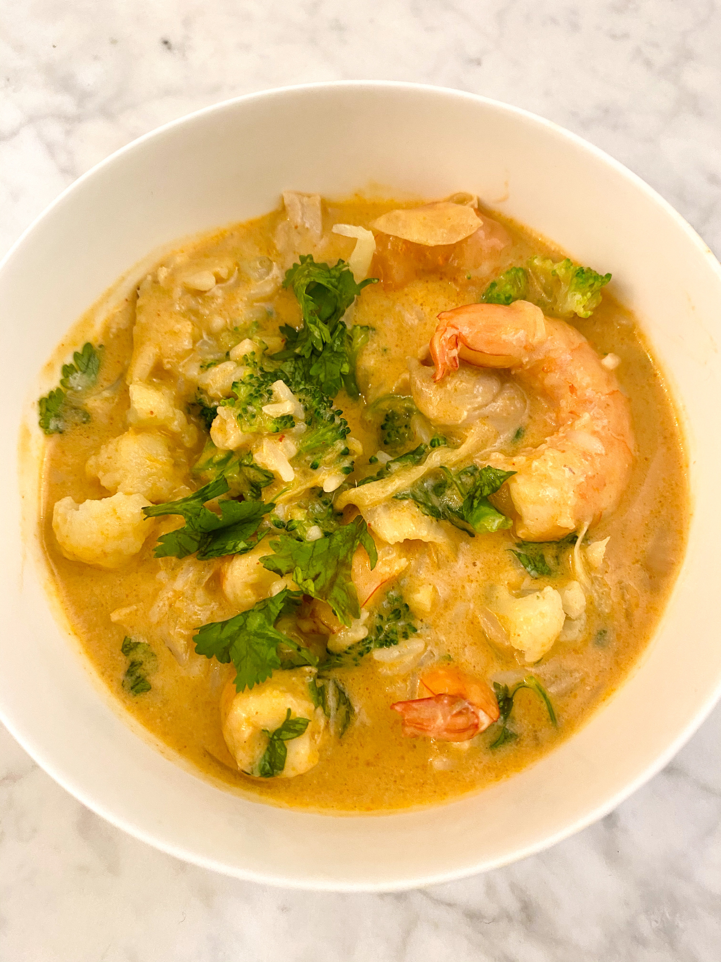 A bowl of shrimp mango coconut curry with cauliflower, broccoli, and herbs.