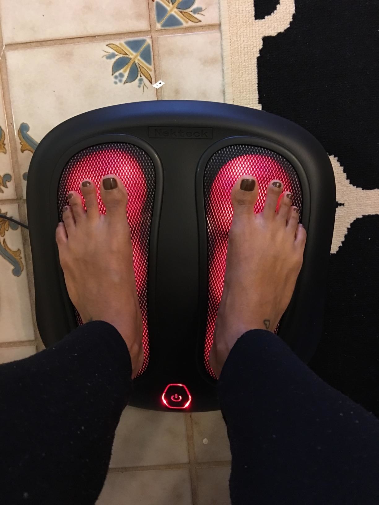 Reviewer places feet on foot massager with red lighting