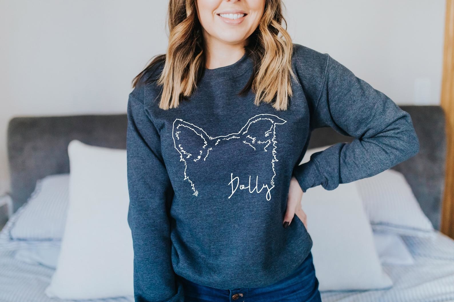 Woman wearing a navy blue version of the sweatshirt with the illustration of outlines of the ears of a dog and the name &quot;Dolly&quot;