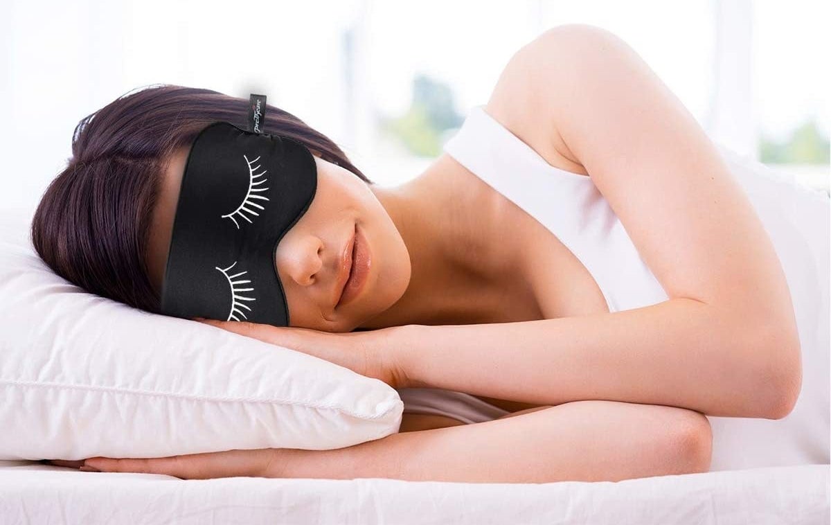 A person sleeps with an eye mask that has eyelashes on it