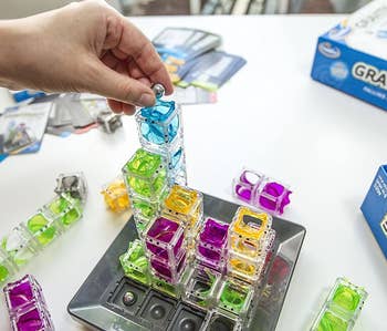 a model placing a marble into the top of clear stacked cubes on the board of the game