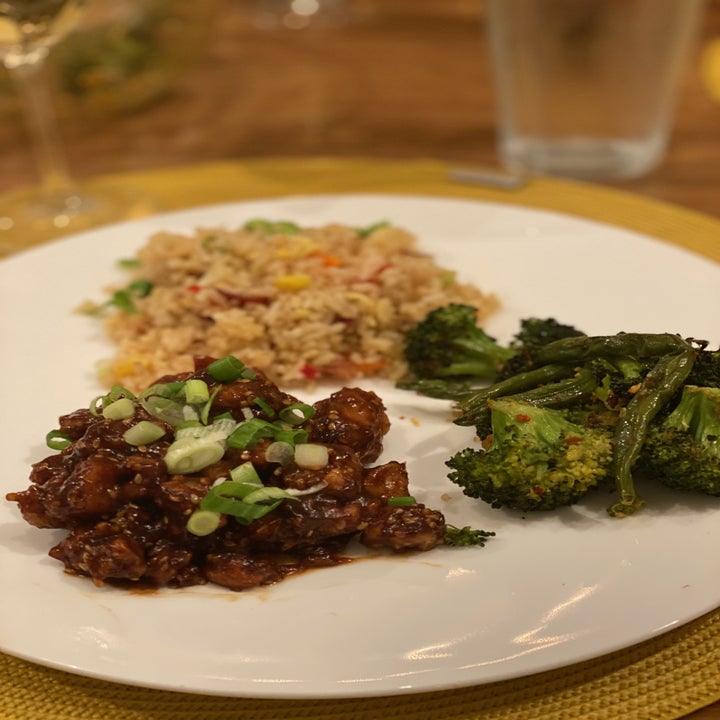 A plate of sesame chicken topped with scallions, fried rice, and broccoli.