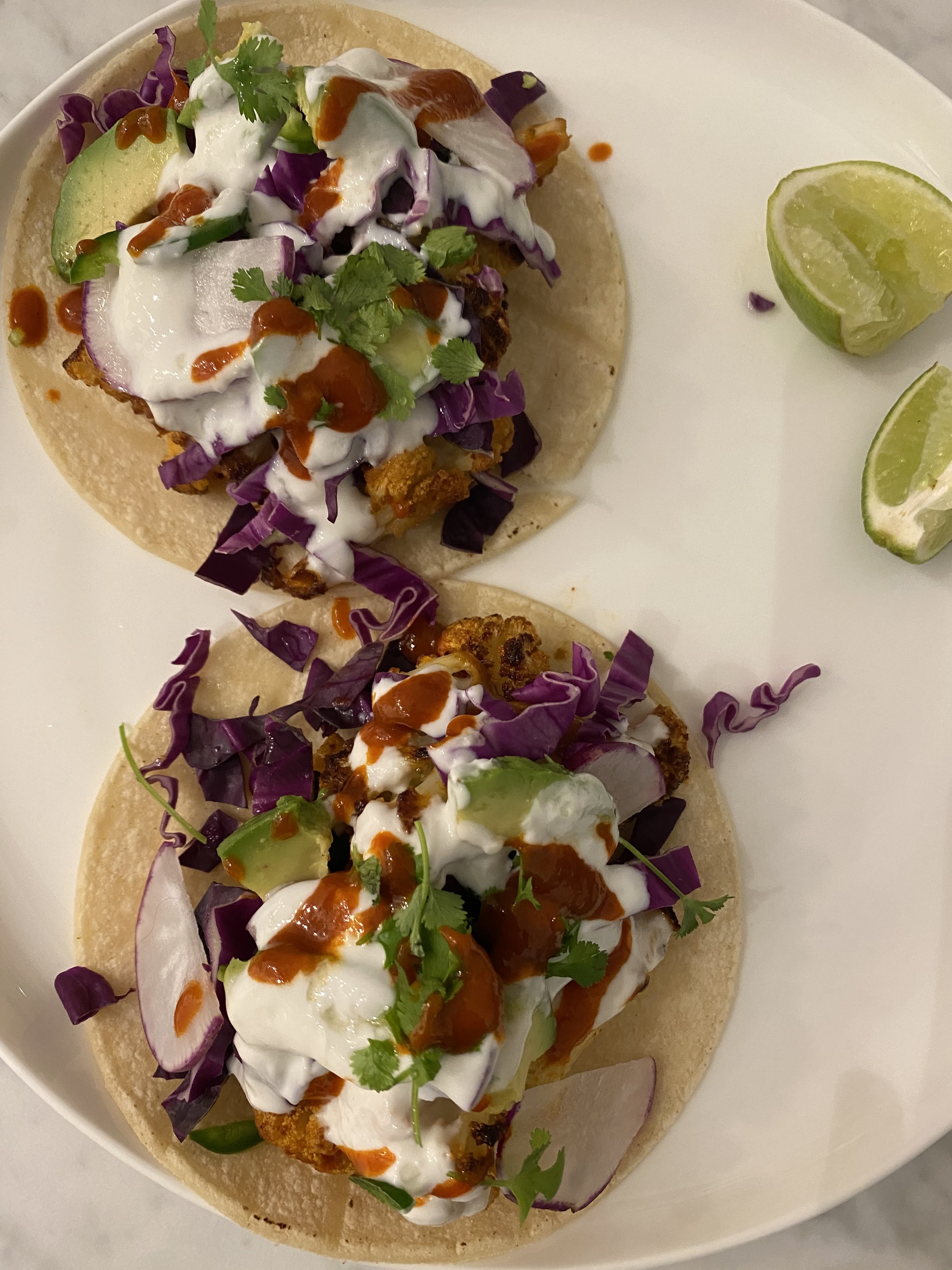 Two chipotle cauliflower tacos topped with cabbage, radish, avocado, and garlic aioli.