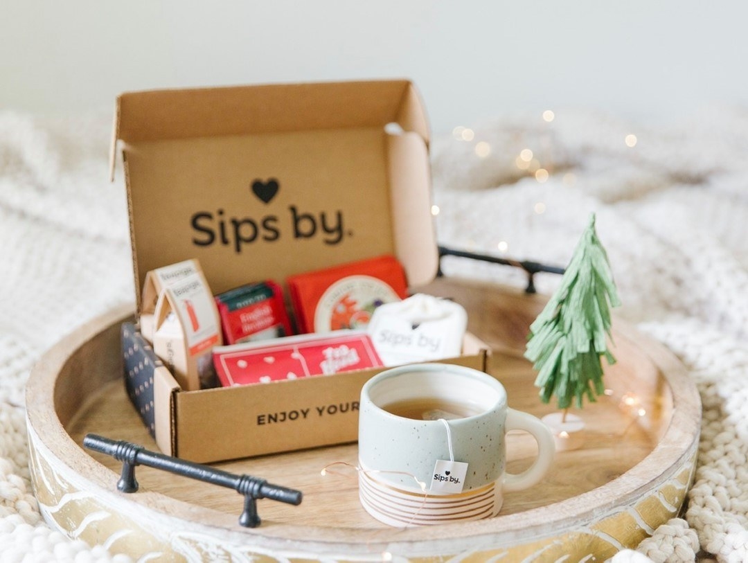 A Sips by box on a tray with a Christmas vibe and a hot cup of tea next to it