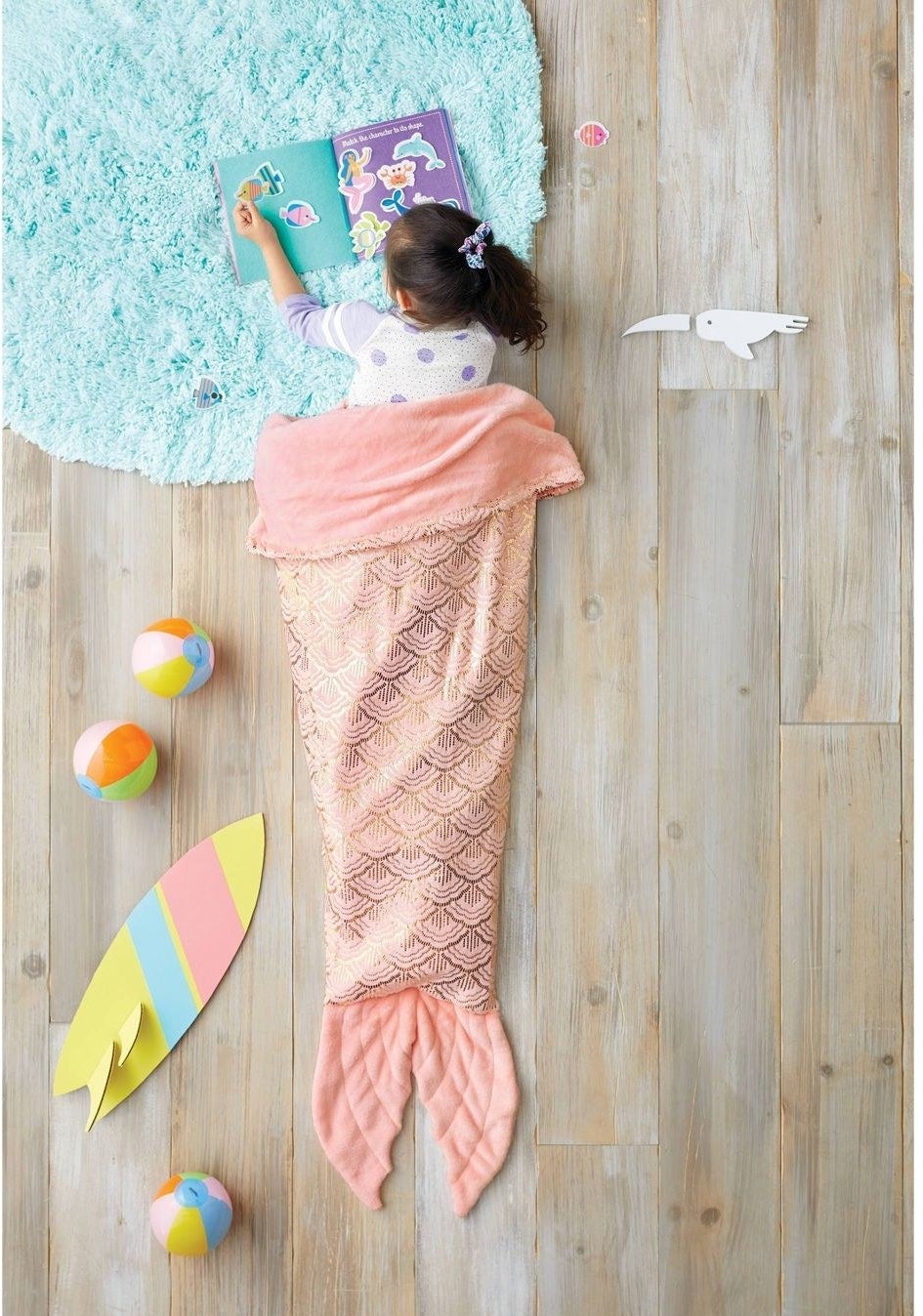 A child wrapped in a sparkly pink blanket that makes them look like they have a mermaid tail