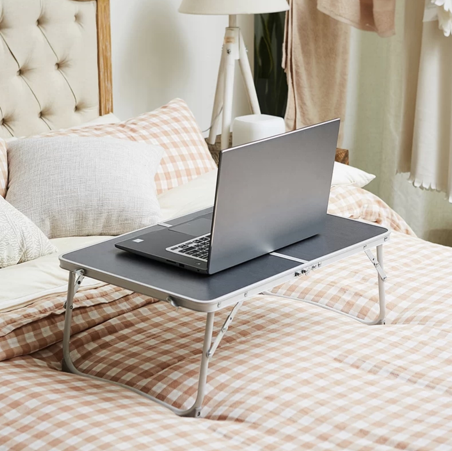A laptop tray with a laptop on top on a bed