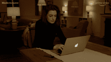 Anne Hathaway swaying her head while typing on a laptop