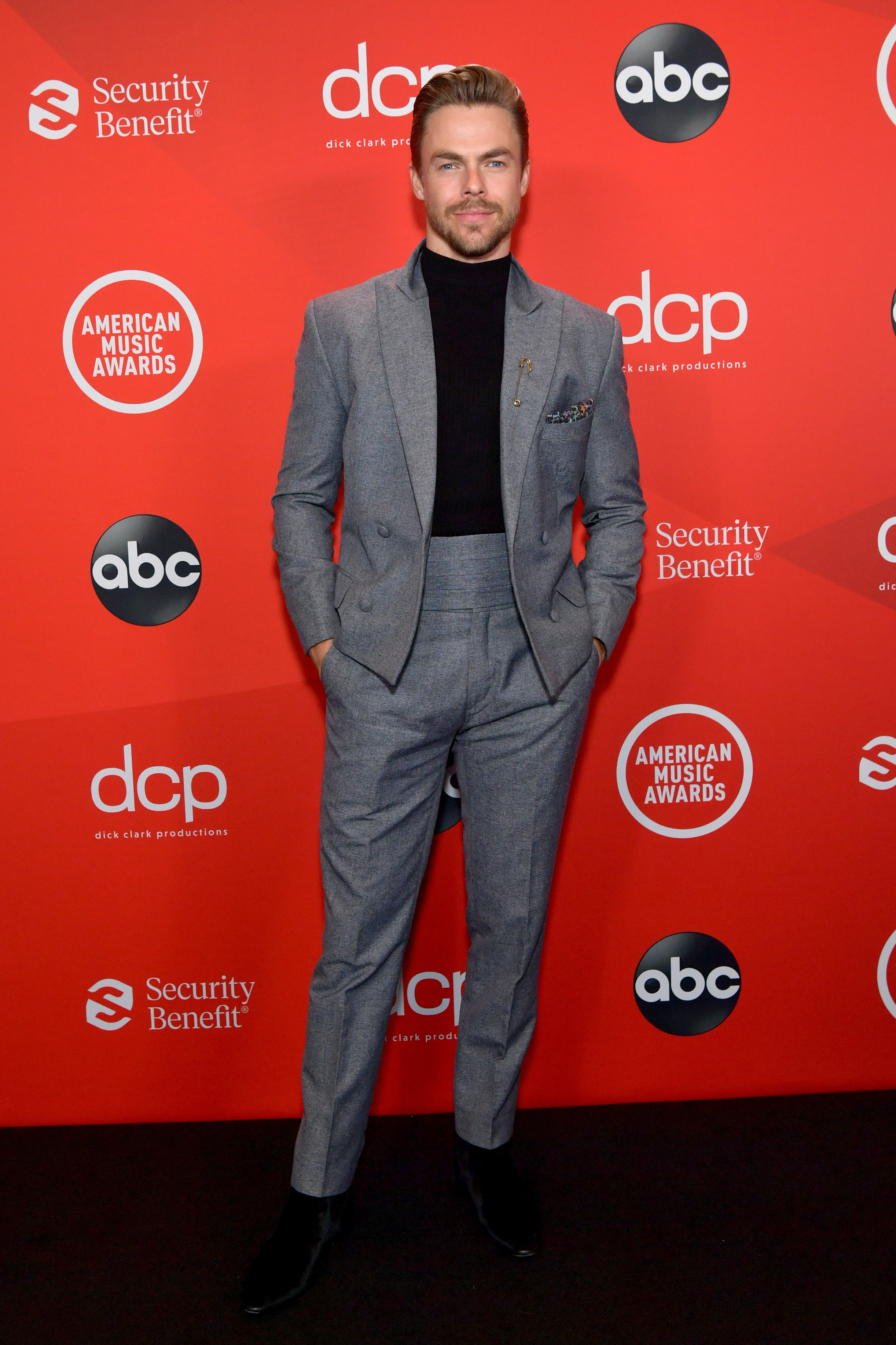 Derek Hough attends the 2020 American Music Awards wearing a jacket and high-waisted pants