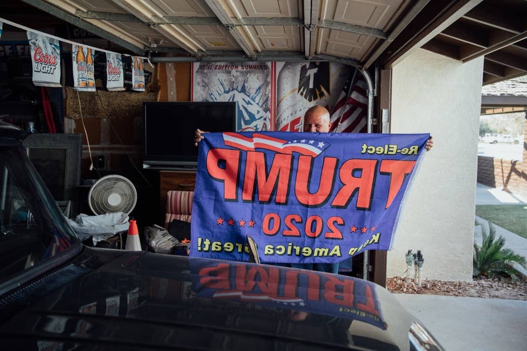 A man in his garage holds up a Trump 2020 flag behind his car