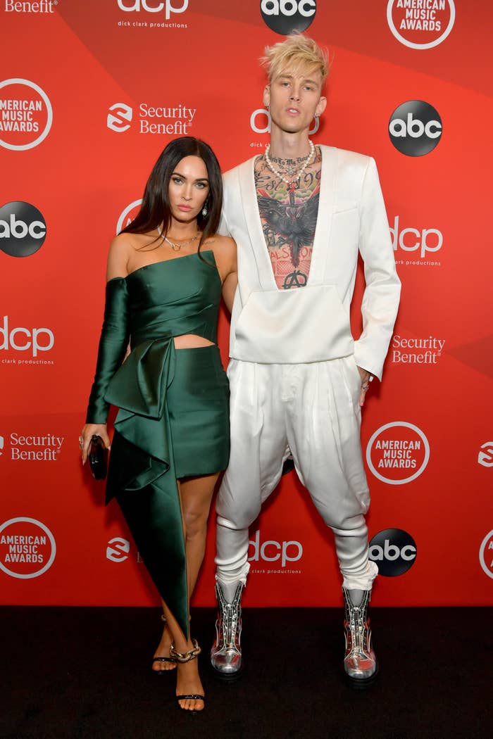 Megan Fox, wearing a one-sleeved dress, and Machine Gun Kelly, wearing a low-cut top and matching harem pants, attend the 2020 American Music Awards
