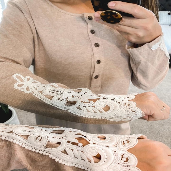 A reviewer wearing the top in tan and holding up their sleeve to show intricate crochet pattern