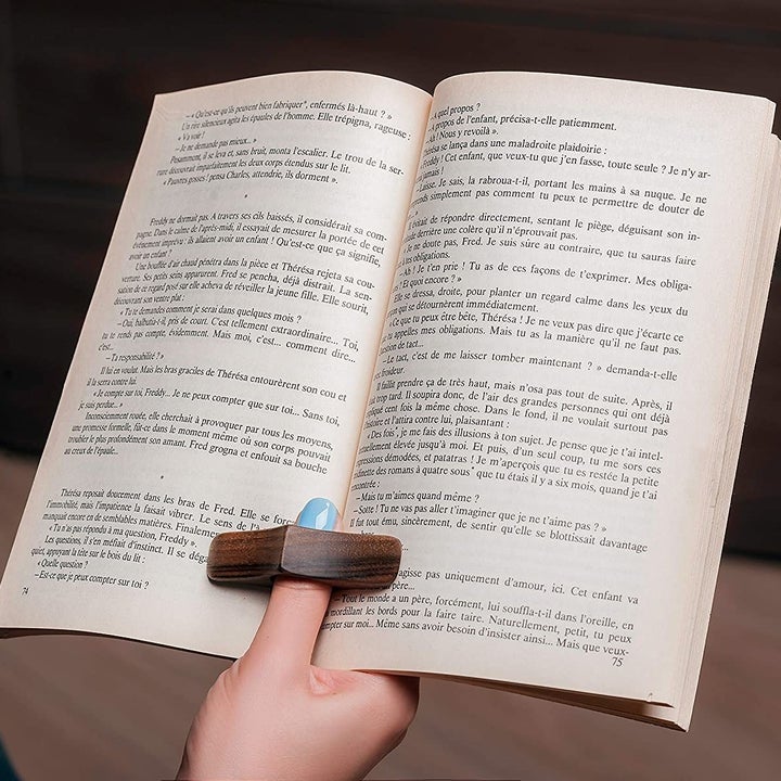 A person holding open a book with the page holder on their thumb