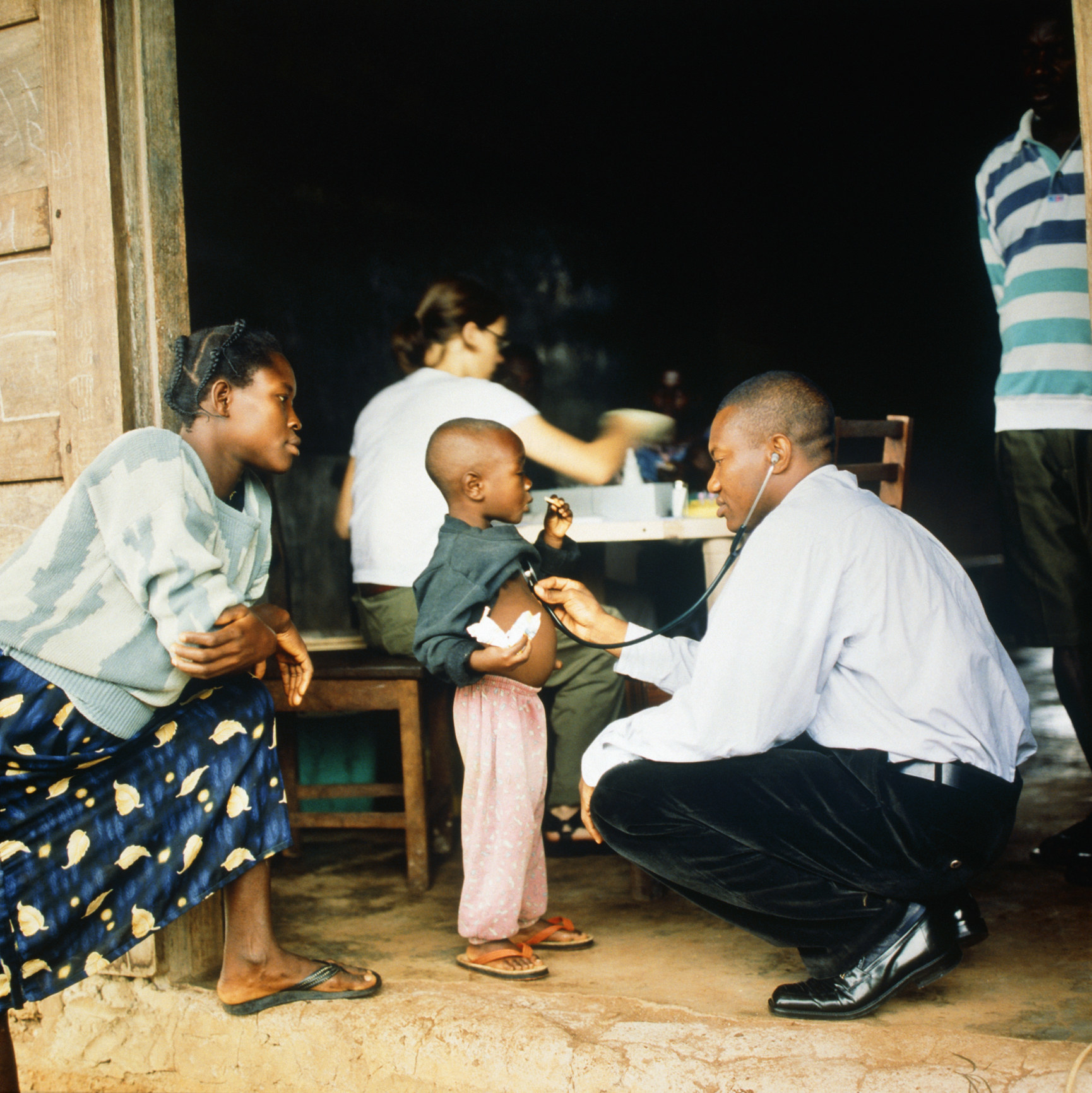 Man checking child&#x27;s heartbeat while mother looks on. 