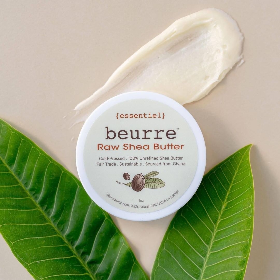 Round container that says &quot;essential beurre raw she butter&quot; next to white shea cream