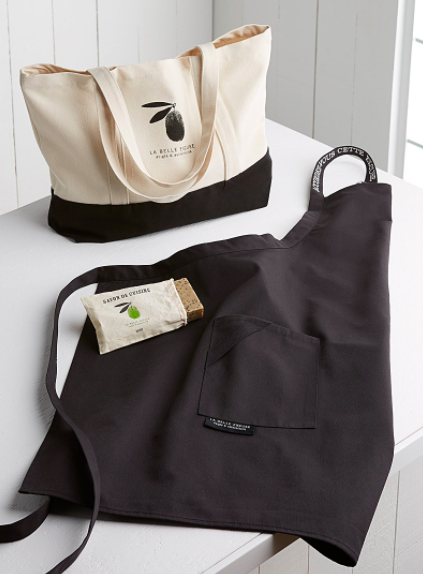 The three piece chef's set consisting of a tote, an apron, and solid soap on a plain kitchen counter