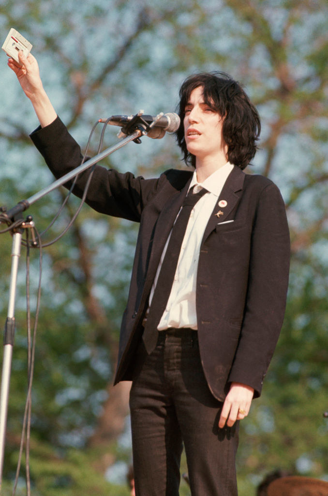 Patti in tight dark jeans and a suit jacket with a button up and tie underneath