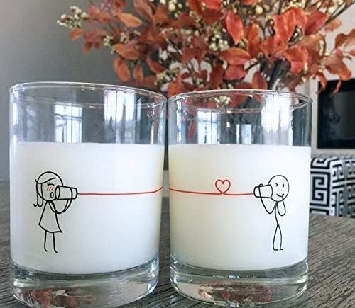 Two clear glasses printed with a scene of two people talking through cans connected with a red string 
