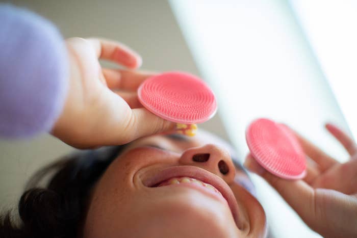 a model playfully holding two face scrubbers up to their eyes
