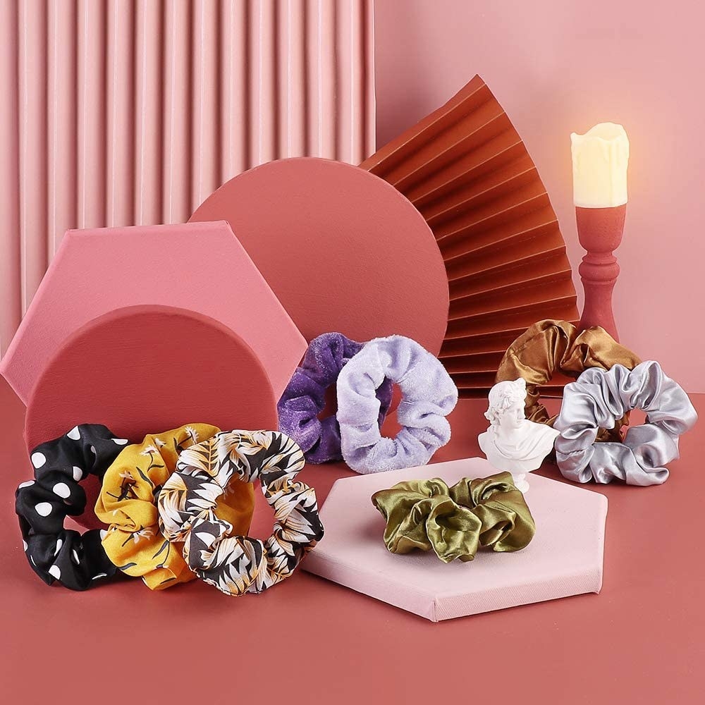 A bunch of scrunchies made of satin and velvet on a table with a tray and a candle