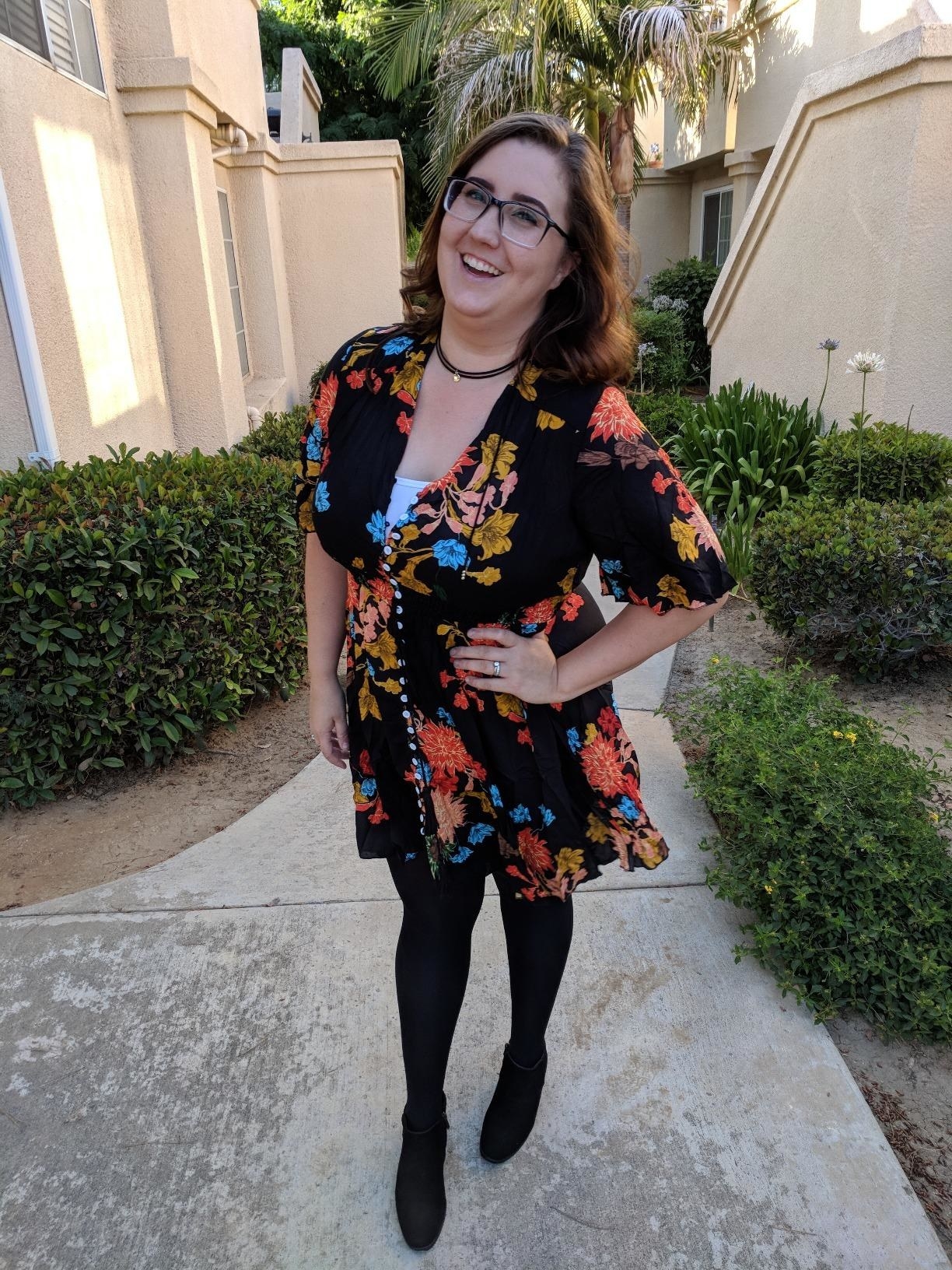 A reviewer wearing the black and colorful floral button-front, short-sleeve dress
