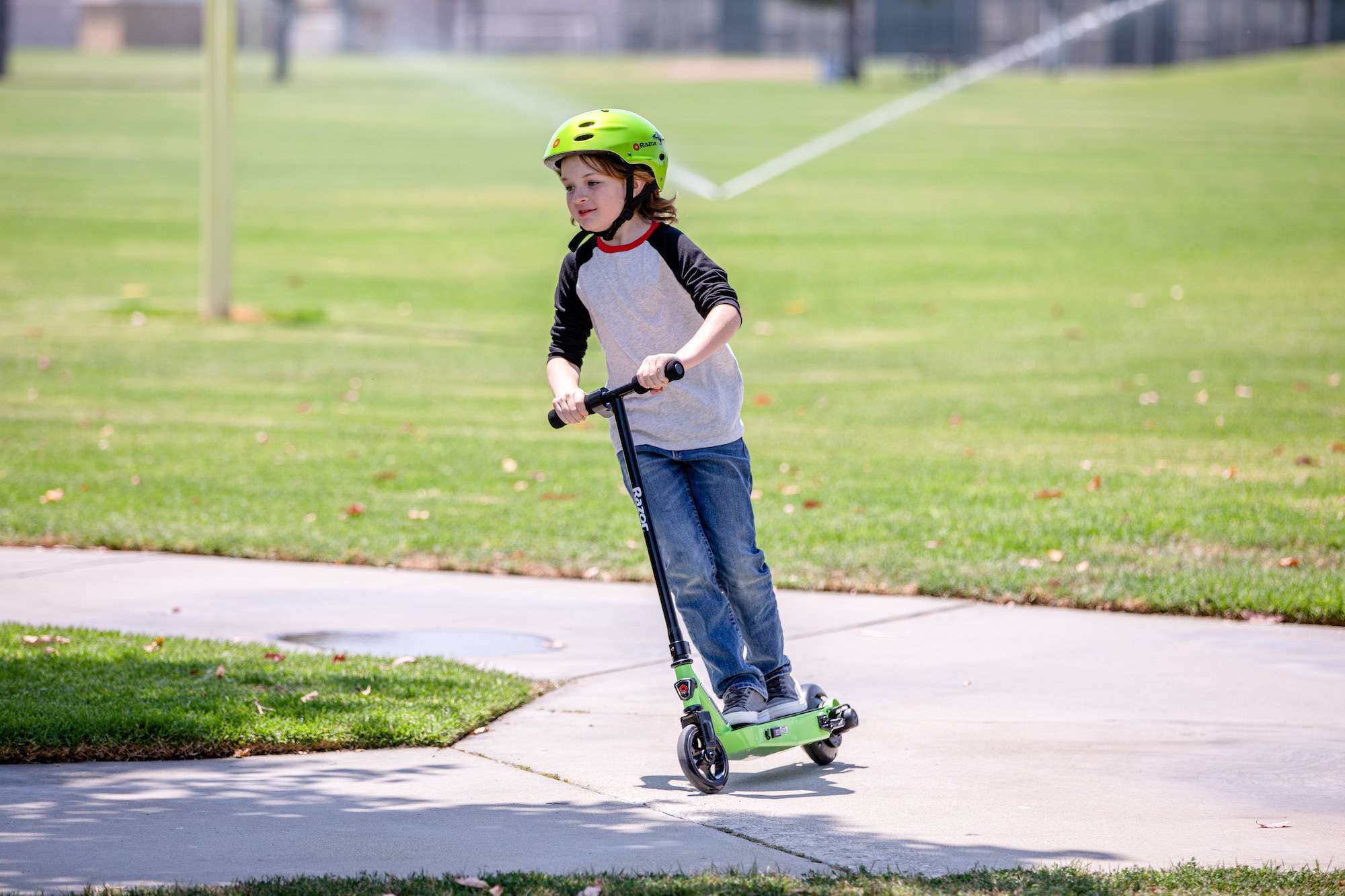 child riding a green razor electric scooter in a park