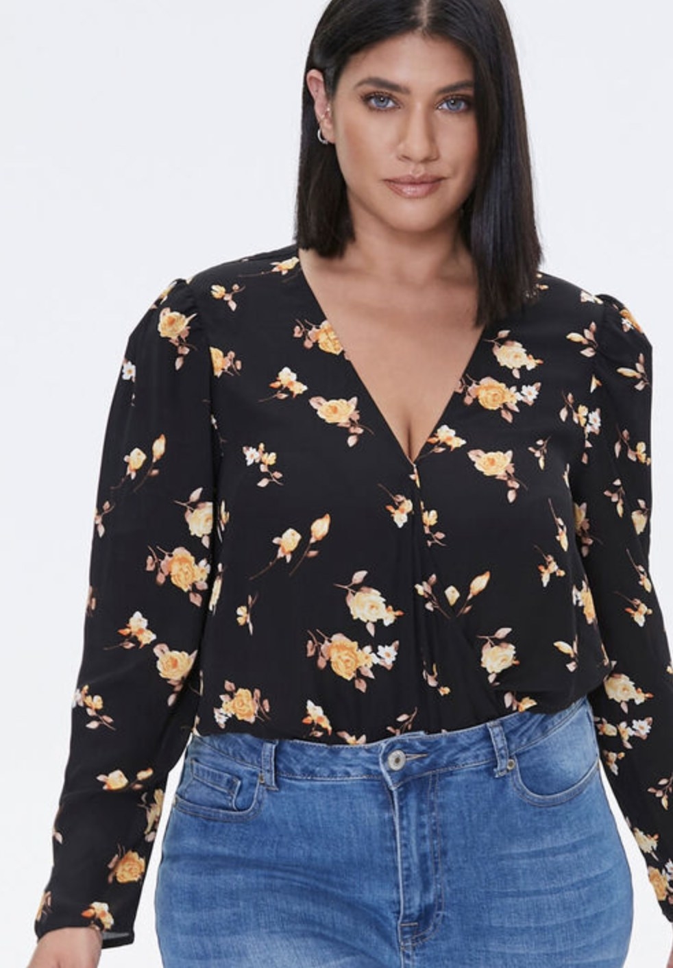 Model is wearing a black and gold floral bodysuit with blue denim jeans